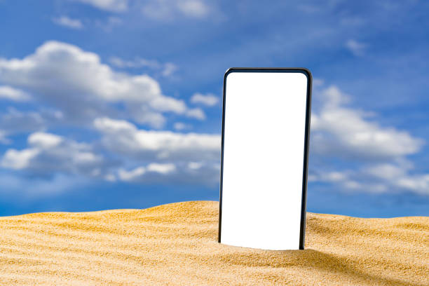 istock Smartphone standing on beach sand with sky at background 1396495587