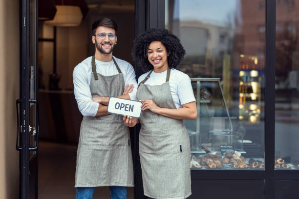 istock Two owners friends holding a open poster together while smiling to the camera in front of pastry shop. 1396501079