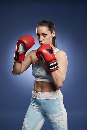Young woman boxer in red boxing gloves, training on blue background