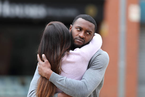 Disappointed man with black skin hugging a woman stock photo