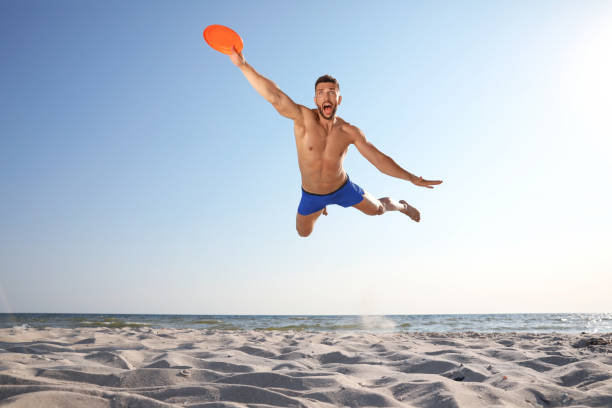 istock Sportive man jumping and catching flying disk at beach 1396506082
