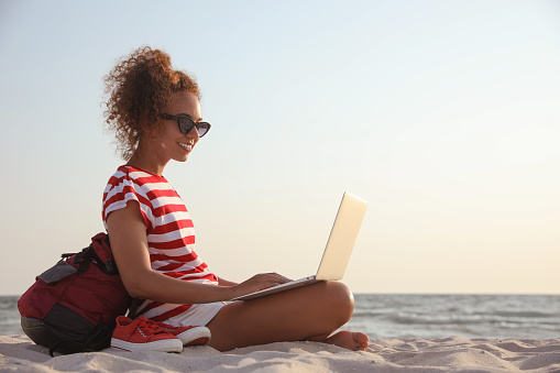 African American woman working on laptop at beach