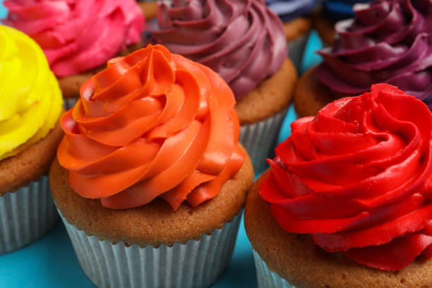 Two cupcakes decorated with orange and yellow cream and festive lights in the background.