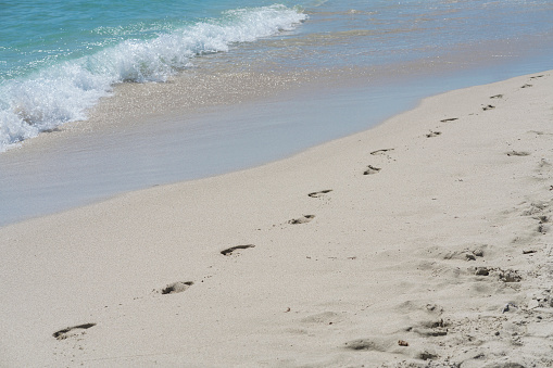 a pair of blue sandals on the beach with beautiful sand. The sandals look natural with traces of human footsteps