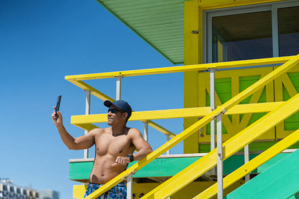 30-year-old Latino man is on vacation on the beaches of Miami 30-year-old Latino man with brown skin dressed in a sun hat and swim trunks without a shirt on vacation on the beaches of Miami enjoying moments alone miami marathon stock pictures, royalty-free photos & images