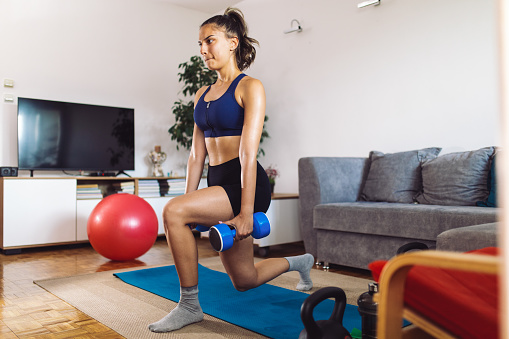Young woman wearing sport clothes and exercising while doing fitness workout in living room at her home.