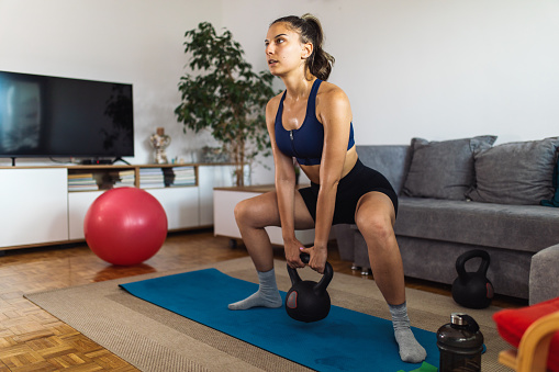 Young woman wearing sport clothes and exercising while doing fitness workout in living room at her home.