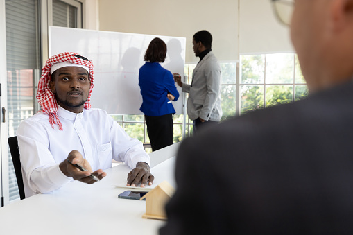 young African muslim businessman in white traditional outfit, talk with colleague in the office