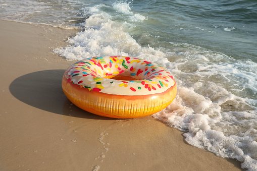 Inflatable ring with doughnut pattern on sandy beach near sea