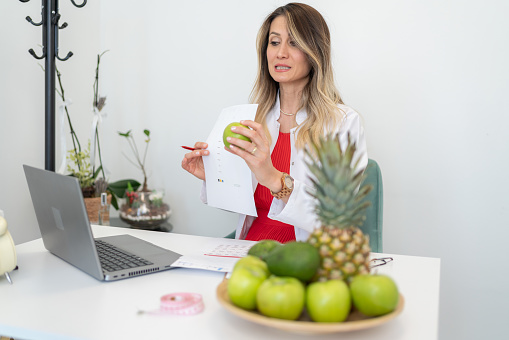 Nutritionist Uses A Laptop To Conduct An Online Consultation With Her Patient At Office