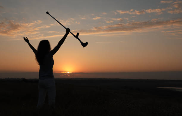 Woman holding elbow crutch outdoors at sunrise, back view. Healing miracle