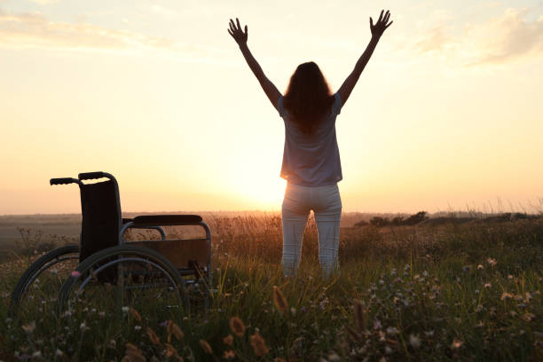 夕方の屋外で車椅子の近くに立っている女性、バッ��クビュー。癒しの奇跡 - physical therapy ストックフォトと画像
