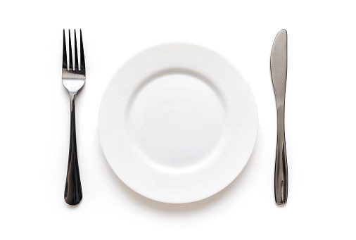 Plate, fork and knife lie on a white tablecloth. The concept of minimalistic table setting, top view.