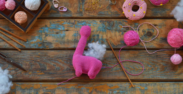 istock Crochet pink dinosaur. Making toy for child. On table threads, needles, hook, cotton yarn. Step 2. Stuff the toy with padding polyester. Handmade crafts. DIY concept. Income from hobby 1396514776