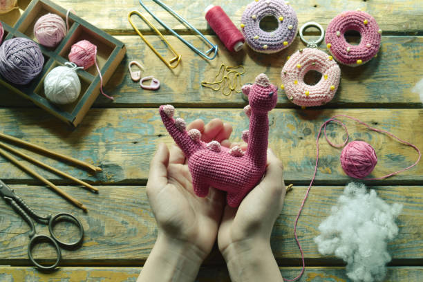istock Crochet pink dinosaur. Making toy for child. On table threads, needles, hook, cotton yarn. Handmade crafts. DIY concept. Small business. Income from hobby 1396514794