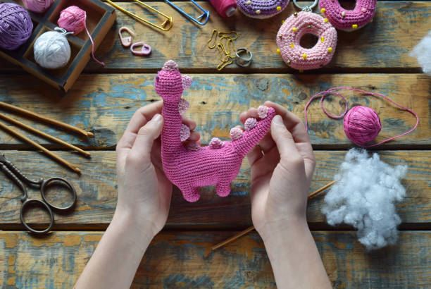 istock Crochet pink dinosaur. Making toy for child. On table threads, needles, hook, cotton yarn. Handmade crafts. DIY concept. Small business. Income from hobby 1396514811