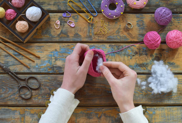 istock Crochet pink dinosaur. Making toy for child. On table threads, needles, hook, cotton yarn. Step 2. Stuff the toy with padding polyester. Handmade crafts. DIY concept. Income from hobby 1396514837