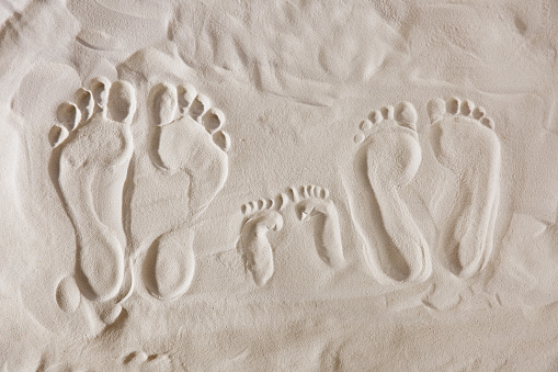 Footprints lead across the sand of an idyllic beach, back lit by the sun at dawn or dusk.