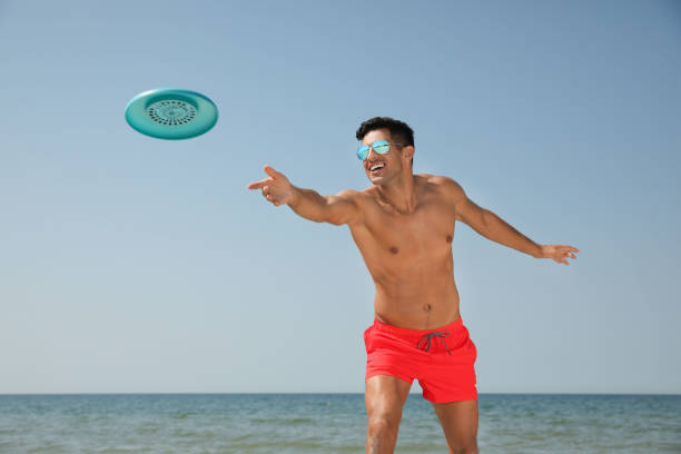 istock Happy man throwing flying disk at beach on sunny day 1396515088