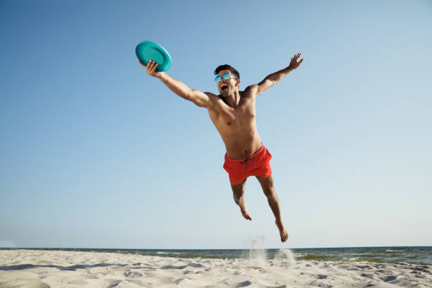 istock Sportive man jumping and catching flying disk at beach 1396515098