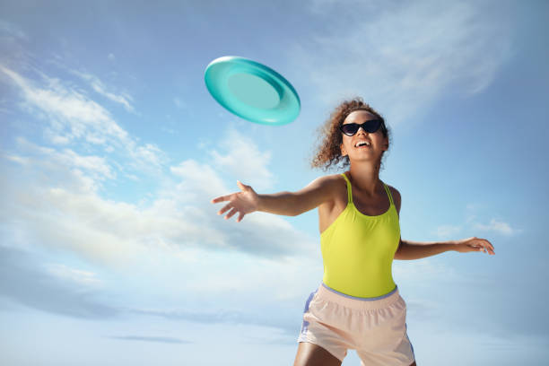 femme afro-américaine heureuse lançant un disque volant contre le ciel bleu par une journée ensoleillée - disque volant photos et images de collection