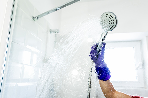 Woman hand with purple glove in the bathroom cleaning the shower