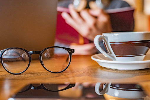 Close-up of reading glasses and cup of coffee on a university desk against male student