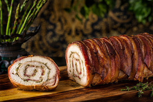 A closeup of bacon rolled pork loin on a wooden cutting board
