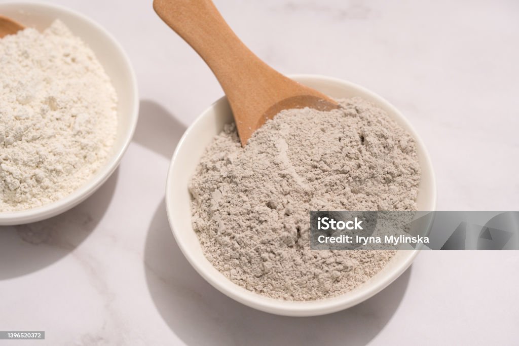 Closeup view of gray and white cosmetic clay on white marble table - mineral powder, bentonite facial mask. Skincare beauty concept. Top view Kaolinite Stock Photo