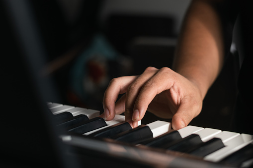 right hand detail of a young latin guy practicing on his piano or electric synthesizer. boy taking virtual lessons at home via internet. song and melody creations as a hobby.