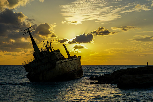 a large old rusty shipwreck silhouette on a rocky coast against a beautiful sunset background