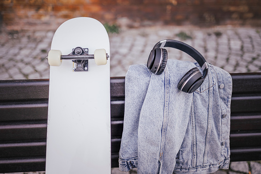 Photo of skateboard, headphones and jacket on park bench