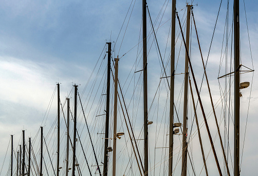 Detail view from the masts of sailboats lined up side by side. Cloudy sky in the background.