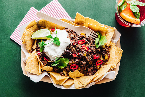 Top view of Mexican traditional nacho chips with minched meat and sour sauce in a plate. Delicious Mexican street food on green table.