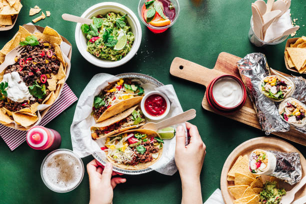 Close-up of a woman serving mexican food and fajitas on green table Close-up of a woman serving mexican street food on green table. Female hands placing a plate of delicious tacos with sauce, nacho chips with minced meat, stuffed tortillas fajitas with sour sauce, and a glass of beer on the table. burrito stock pictures, royalty-free photos & images