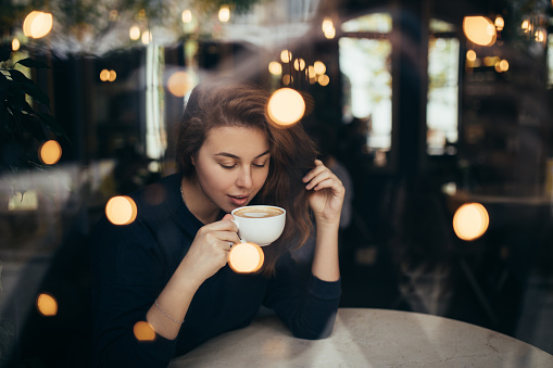 Young woman sitting in a cozy coffehouse drinking coffee near window.