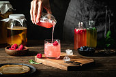 Close-up of woman pouring raspberry kombucha tea in glass