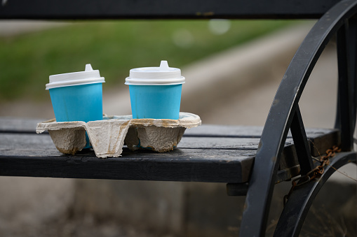 Two blue paper cups of coffee left on a street bench.