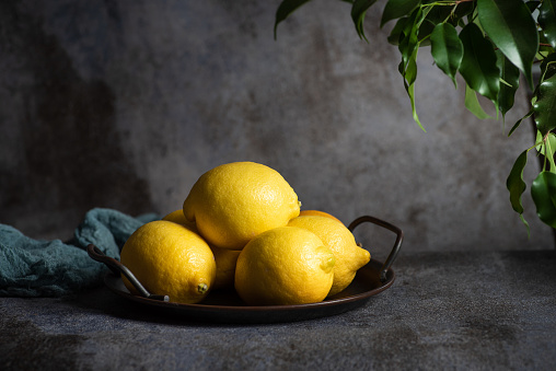 Fresh organic lemon in a bowl on a rustic black-gray background with copy space