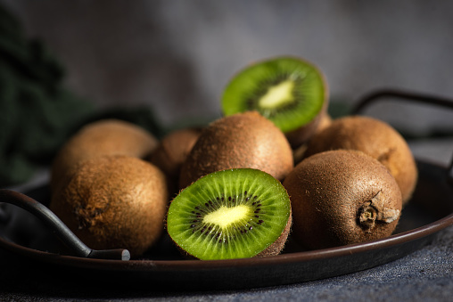 Fresh whole and sliced kiwi fruit in a metal bowl on a black and gray background
