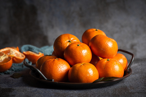 Fresh whole and sliced tangerines on a gray background in a metal bowl on a black-gray background