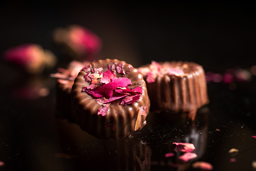 Homemade pralines made of dark chocolate sprinkled with rose petals on a dark background