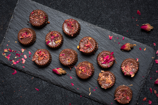 Homemade pralines made of dark chocolate sprinkled with rose petals on a dark background