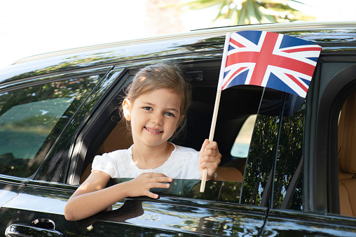 Girl in car is holding British flag with a toothy smile.