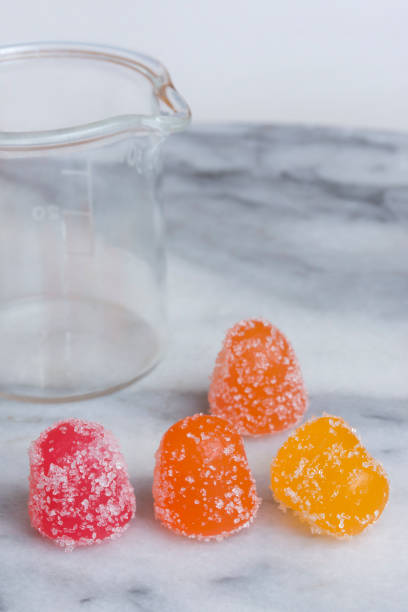 CBD gummy candy gumdrops and beaker on a white marble surface stock photo