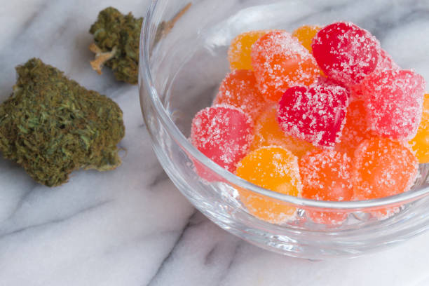 CBD gummy candy gumdrops and buds on a white marble surface stock photo