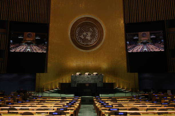 United Nations General Assembly chamber, front view of the podium with a UN emblem Empty hall of the United Nations General Assembly at the UN headquarters in New York during the Assembly's 76th regular session on February 2, 2022. The chamber has frequently been found empty during the COVID-19 pandemic period due to meeting restrictions imposed by the Host Government. summit meeting photos stock pictures, royalty-free photos & images