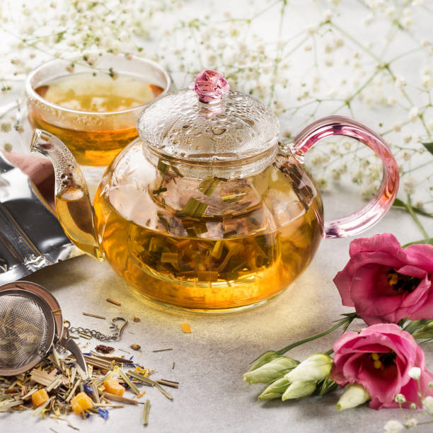 Hot lemongrass tea in a glass teapot on a light background decorated with flowers stock photo