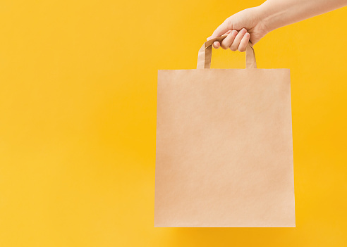 Woman is holding paper bag with handles on yellow backdrop