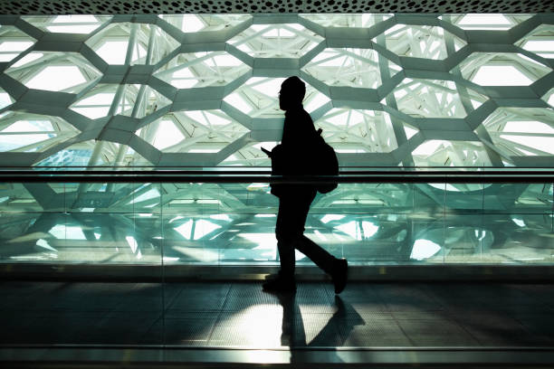 Young man with a backpack walking across reflective floor with multi paneled windows in the background, monochrome